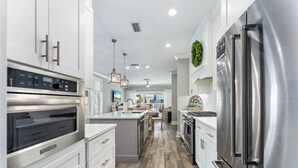 A modern kitchen with stainless steel appliances, white cabinetry, and a central island. - Golf Cart, Pool, Deck, Grill, & Beach Gear (Mexico Beach)