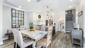 A spacious kitchen with a central island, white cabinetry, and a dining area with striped chairs and a wooden table. - Golf Cart, Pool, Deck, Grill, & Beach Gear (Mexico Beach)