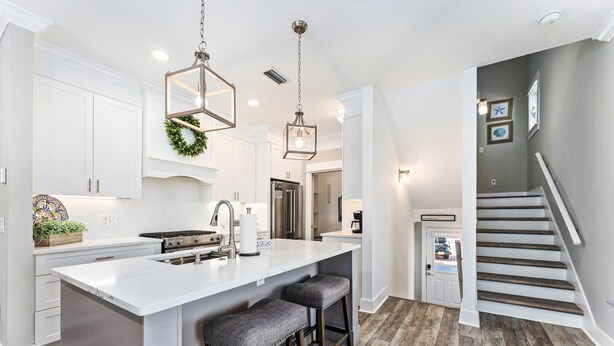 A modern kitchen with white cabinetry, a central island with bar stools, stainless steel appliances, and pendant lighting. - Golf Cart, Pool, Deck, Grill, & Beach Gear (Mexico Beach)
