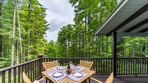 Eine Holzterrasse mit Esstisch, umgeben von hohen Bäumen.