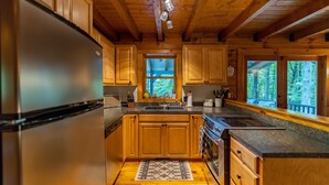 Eine Küche mit Holzschränken, einem Edelstahlkühlschrank, einer Granitabdeckung und einem Fenster mit Blick auf einen Wald.