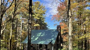 Eine Holzhütte mit Steinkamin, umgeben von einem Wald im Herbstlaub.