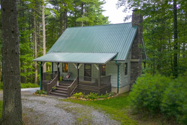 A cabin with a metal roof, wooden porch, and stone chimney, surrounded by dense forest. - Perfect Cabin in the Woods! Hot Tub, Fire Pit, WI-FI, Central A/C (Sparta)