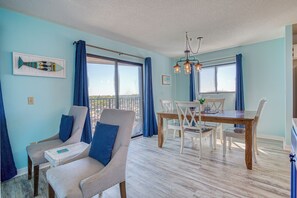 A room with a dining table, chairs, a chandelier, and a large window with curtains. - Beautiful Ocean View Condo, Pools, Lazy River, Hot Tub, Playground, Tennis Court (Myrtle Beach)