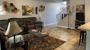 Un salon avec un canapé en cuir, une table basse et un tapis. Un escalier mène à un autre niveau.