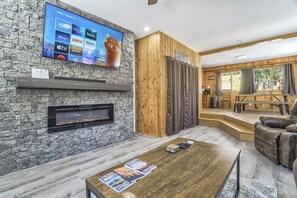 A modern living room with a stone fireplace, a flat-screen TV mounted on the wall, and a wooden door labeled "FRIDAY". - Colorado Mountain House - Views and a Hot Tub! (Cascade-Chipita Park)