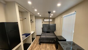 Ein kleines Zimmer mit Küchenzeile, einem Bett, einem Fernseher und einem begehbaren Kleiderschrank.