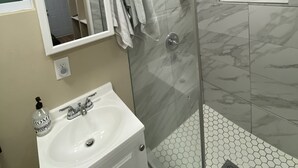 Ein modernes Badezimmer mit einer gläsernen Duschkabine, einem weißen Waschbecken und einem Spiegel darüber.