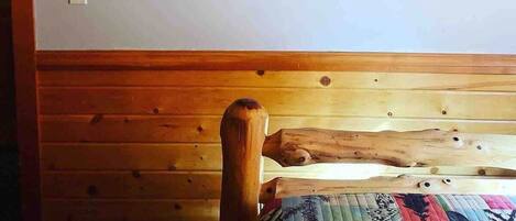 Ein Zimmer mit einem hölzernen Kopfende, einer Steppdecke und zwei gerahmten Postern an der Wand.