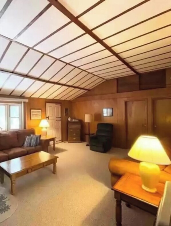 A cozy living room with a high ceiling, wooden paneling, a sofa, a coffee table, a lamp, and a chair.