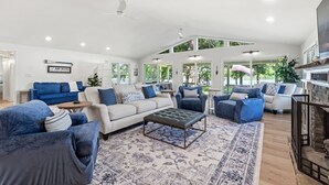 Een ruime woonkamer met een grote bank, fauteuils, een salontafel en een open haard.