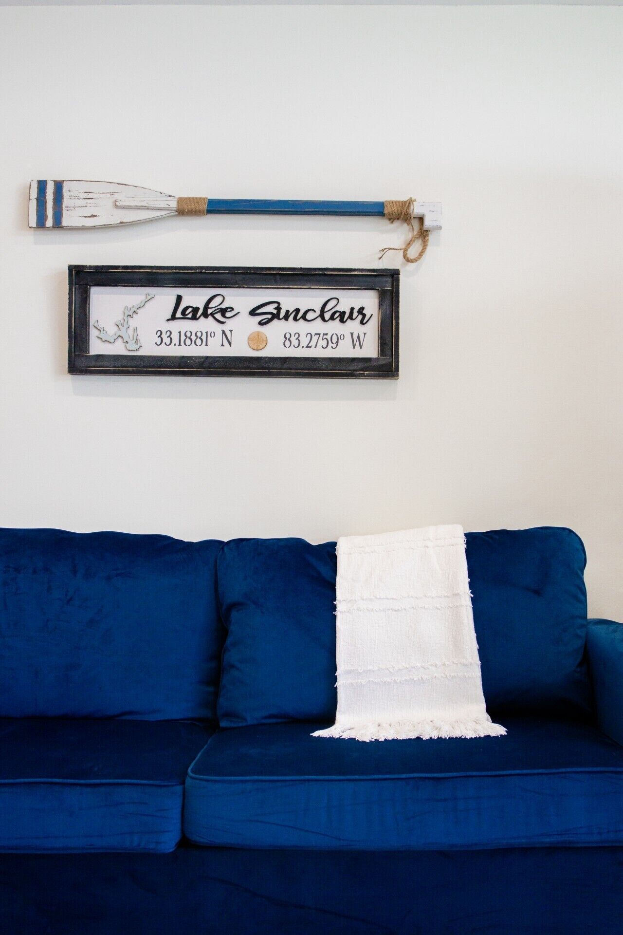 Un canapé bleu surmonté d’un plaid blanc, un panneau encadré indiquant des coordonnées géographiques et un objet décoratif placé au-dessus.