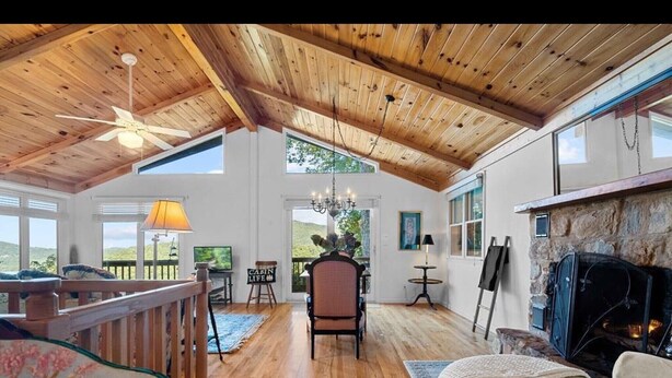 A spacious living area with wooden floors, a fireplace, and large windows offering views of the outdoors. - Stunning panoramic mountain views-close to town! (Highlands)