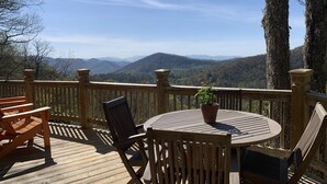 A wooden deck with a round table and chairs, overlooking a mountainous landscape. - Stunning panoramic mountain views-close to town! (Highlands)