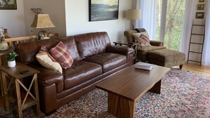 A cozy living room with a brown leather sofa, a wooden coffee table, and patterned rugs. - Stunning panoramic mountain views-close to town! (Highlands)