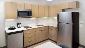 A compact kitchen with wooden cabinets, a stainless steel refrigerator, a microwave, a dishwasher, and a sink.