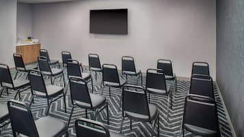 A conference room with rows of chairs, a flat-screen TV on the wall, and a patterned carpet.