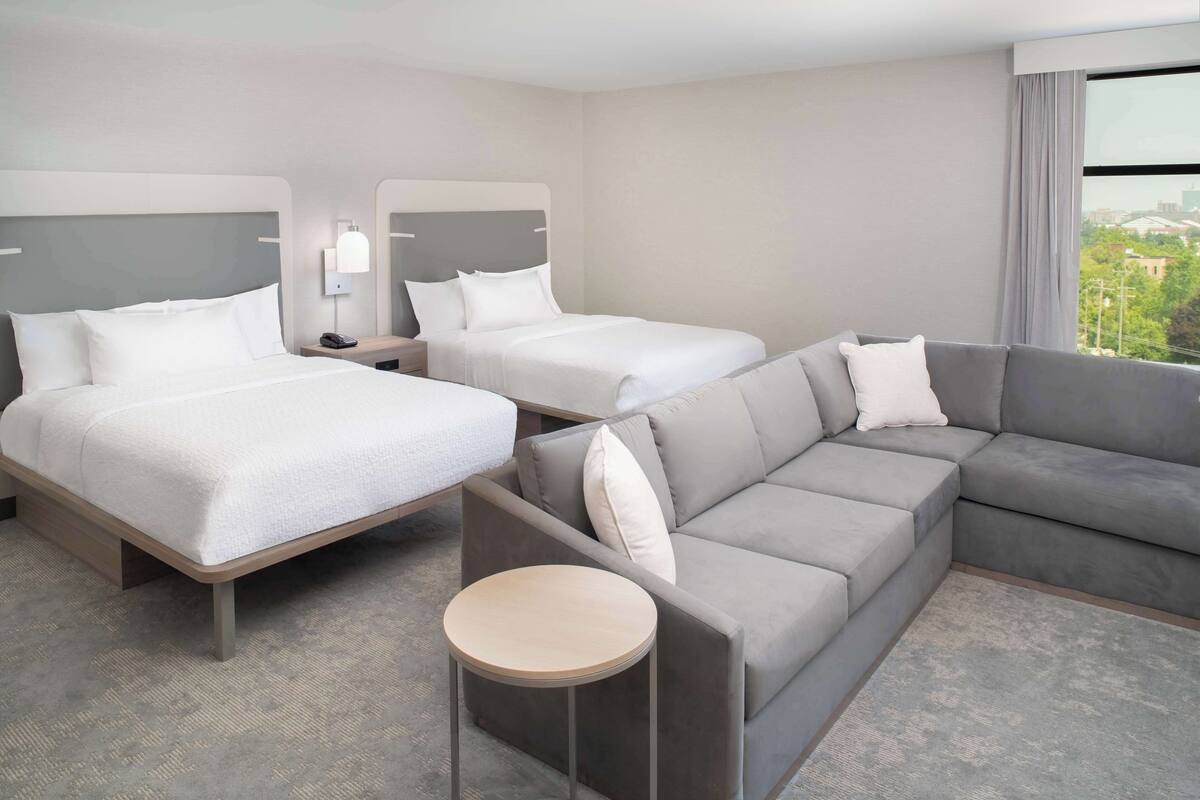 Habitación de hotel con dos camas, un sofá, una mesa redonda y vistas a la ciudad.