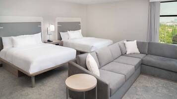 A hotel room with two beds, a sofa, a round table, and a city view.