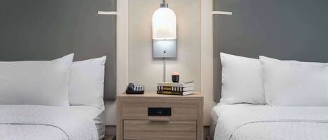 A hotel room with two beds, a bedside table with a lamp, and a small drawer.
