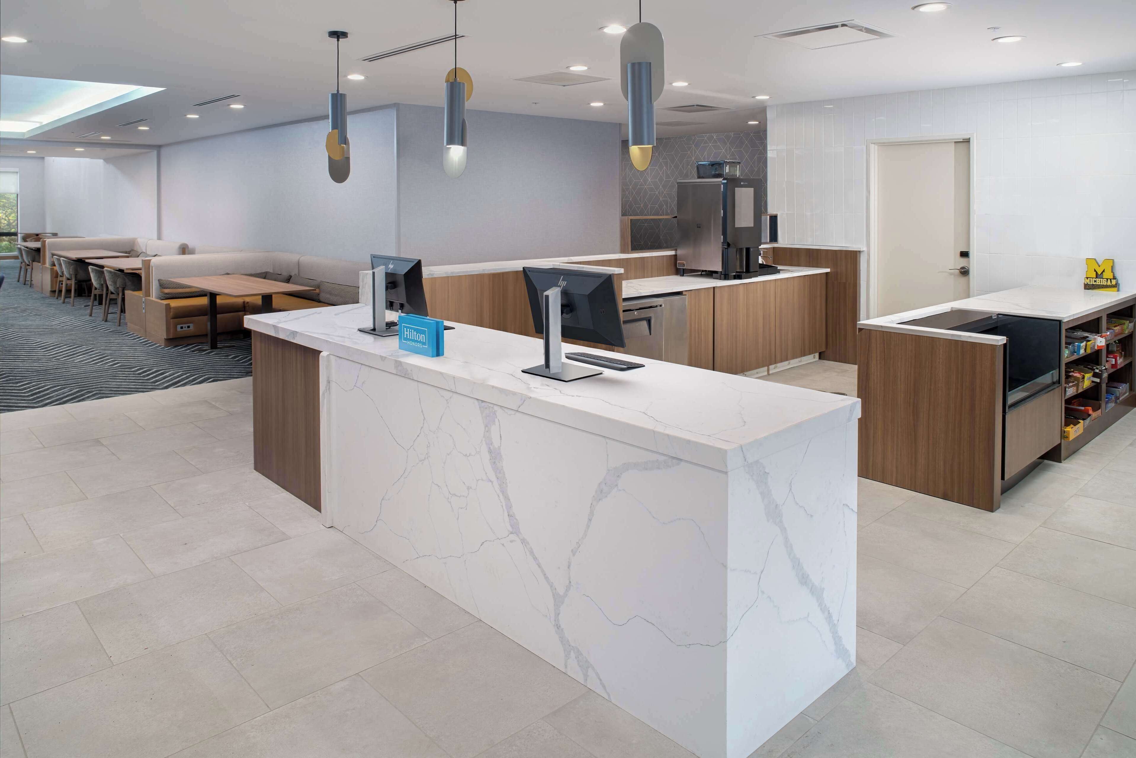 A modern hotel lobby with a marble reception desk, seating area, and a kitchenette.