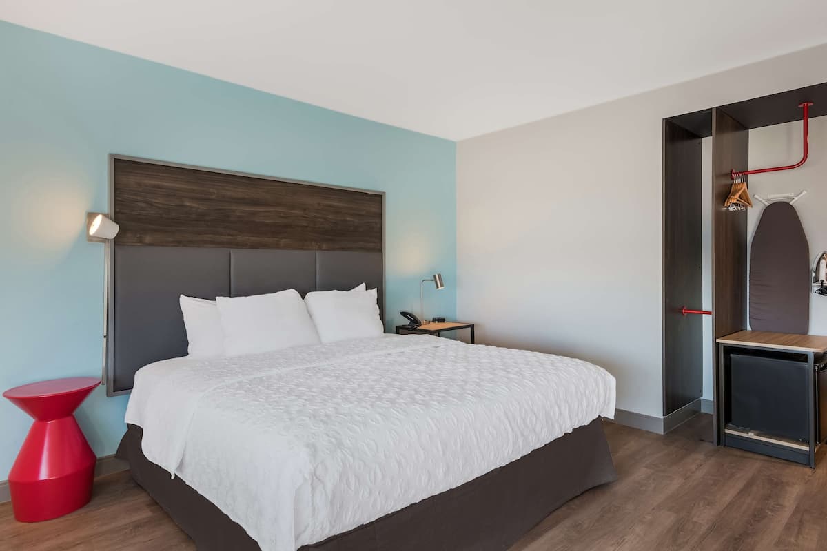 Une chambre d’hôtel moderne avec un grand lit, une table de chevet rouge, une lampe de chevet et une armoire avec un miroir.