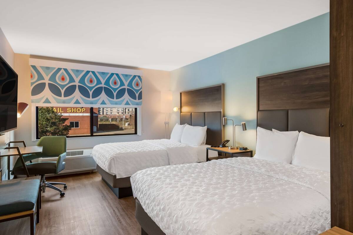 Une chambre d’hôtel avec deux lits, un bureau, une chaise, une télévision et un mur sur lequel est affiché un panneau indiquant « Salon d’onglerie ».