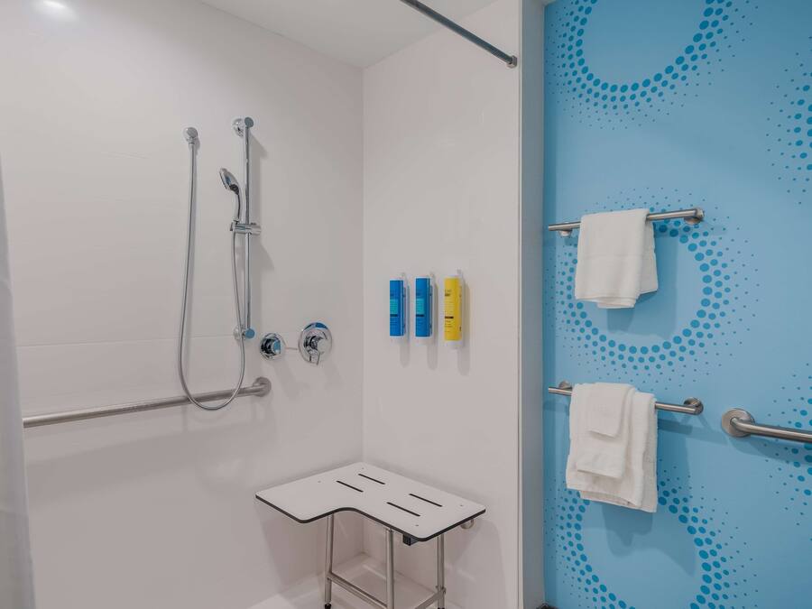 A shower area with a white shower tray, handheld showerhead, and a wall-mounted faucet. There are three toiletry bottles on the wall and two towels on towel bars.