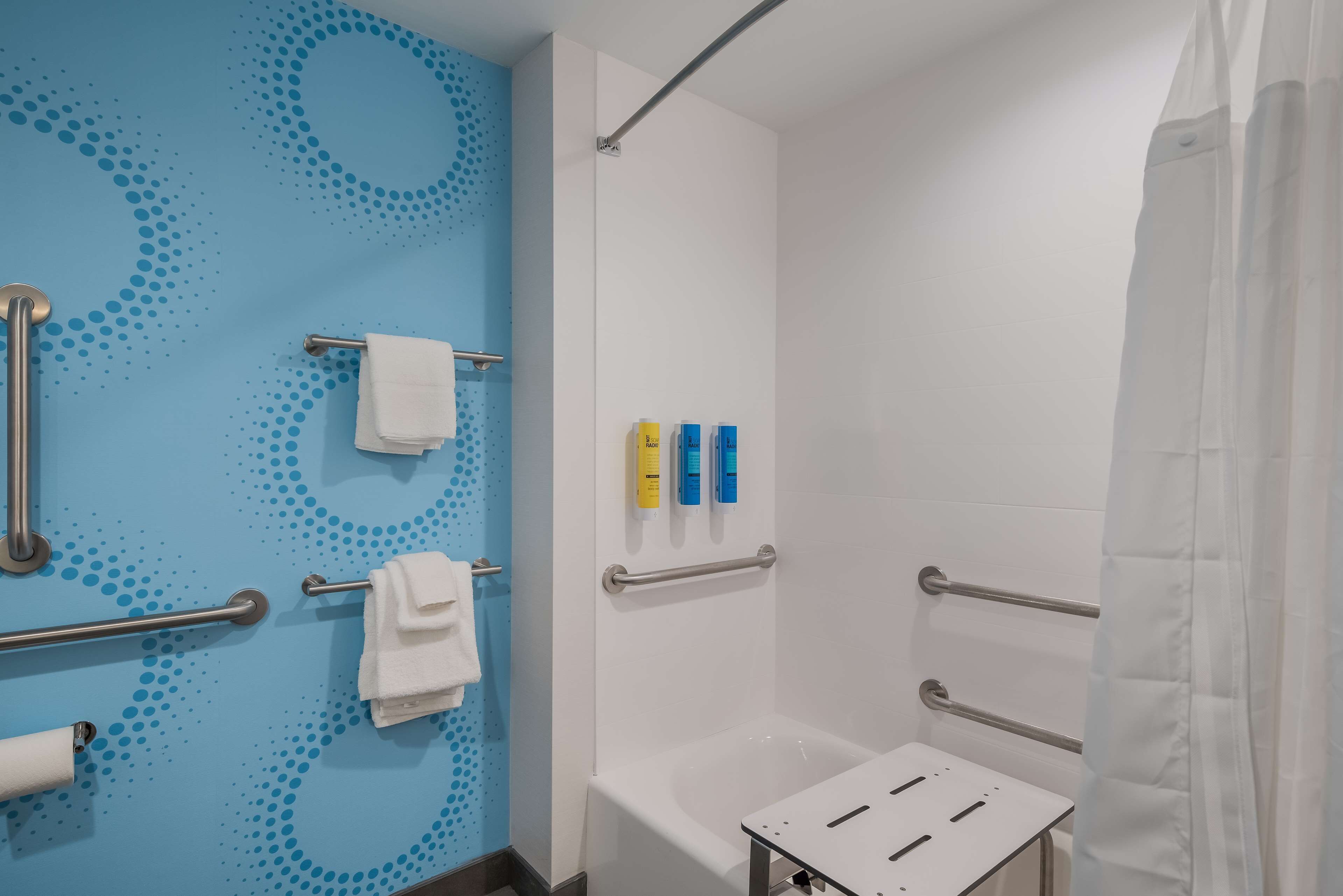 Un baño moderno con pared de diseño azul, una bañera blanca y barras de apoyo.