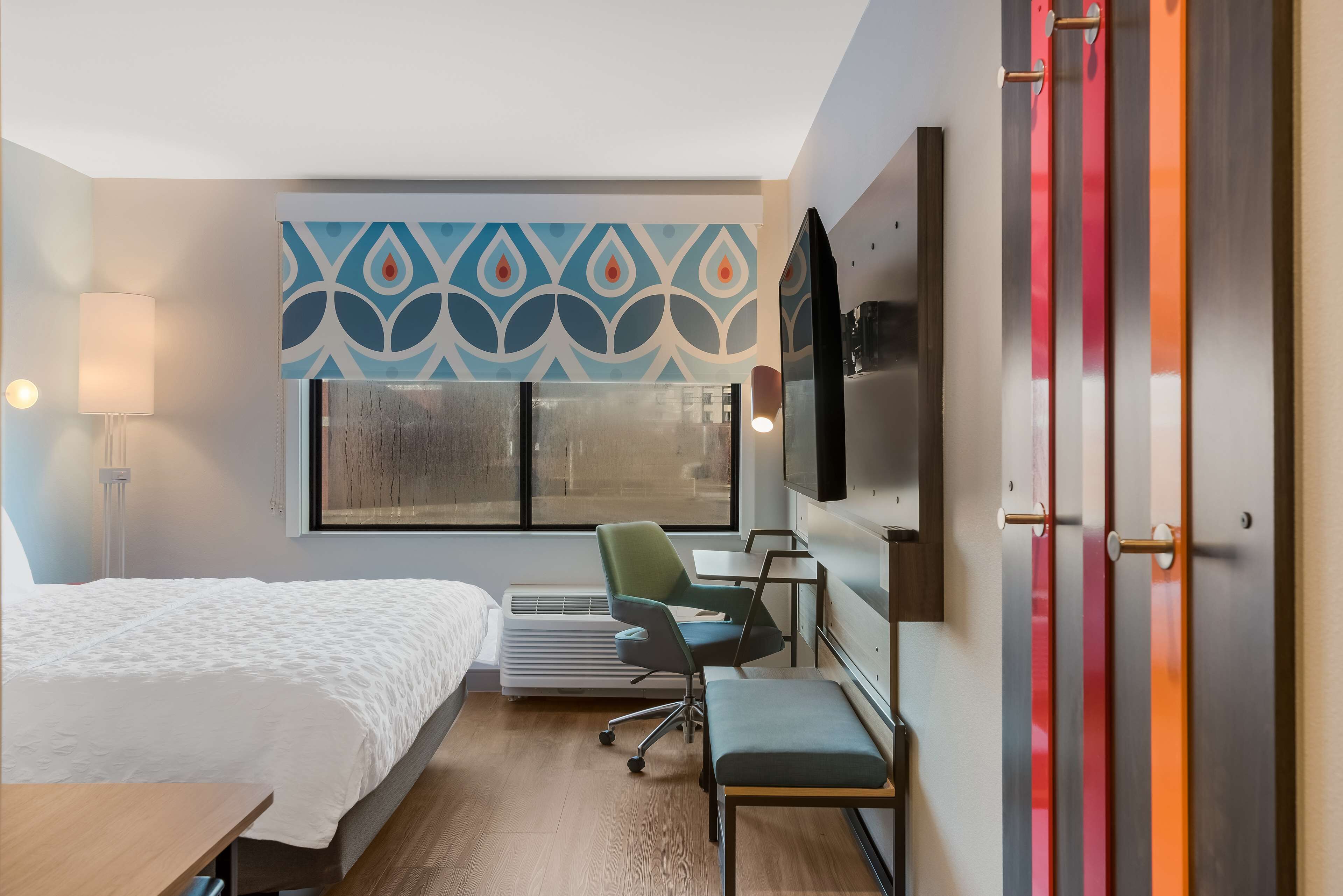 A hotel room with a bed, desk, chair, and a TV on the wall.