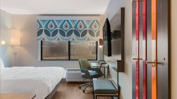 A hotel room with a bed, desk, chair, and a TV on the wall.