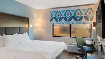 Ein Hotelzimmer mit einem großen Bett, einem Schreibtisch mit Stuhl, einem Fenster mit Blick und einer Wand mit dekorativem Muster.