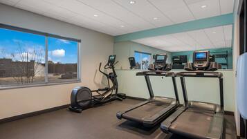 A fitness room with treadmills, an elliptical, and a large window with a view of the outside.