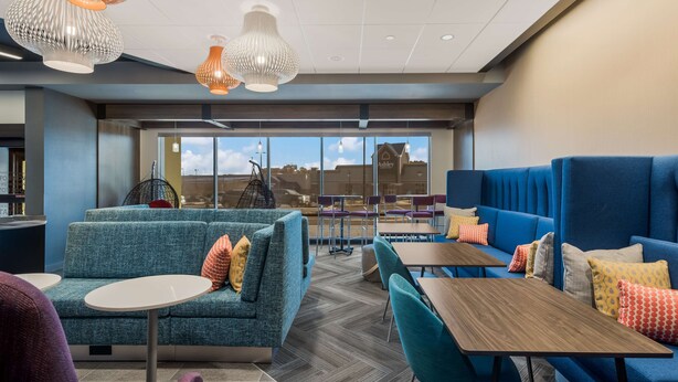 A modern lounge area with blue seating, white tables, and pendant lighting. - Tru by Hilton Greensboro, NC (Greensboro)