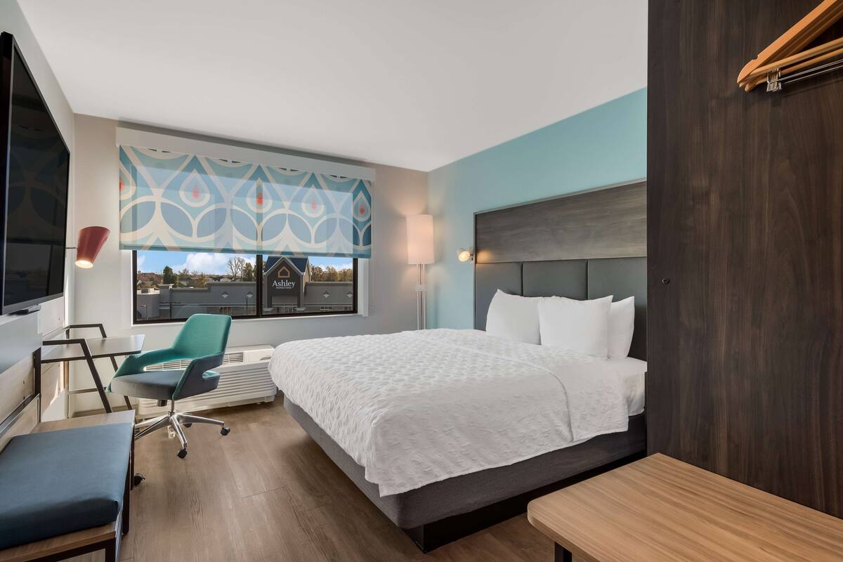 Une chambre d’hôtel moderne, dotée d’un grand lit, d’un bureau, d’une chaise et offrant une vue sur l’extérieur.