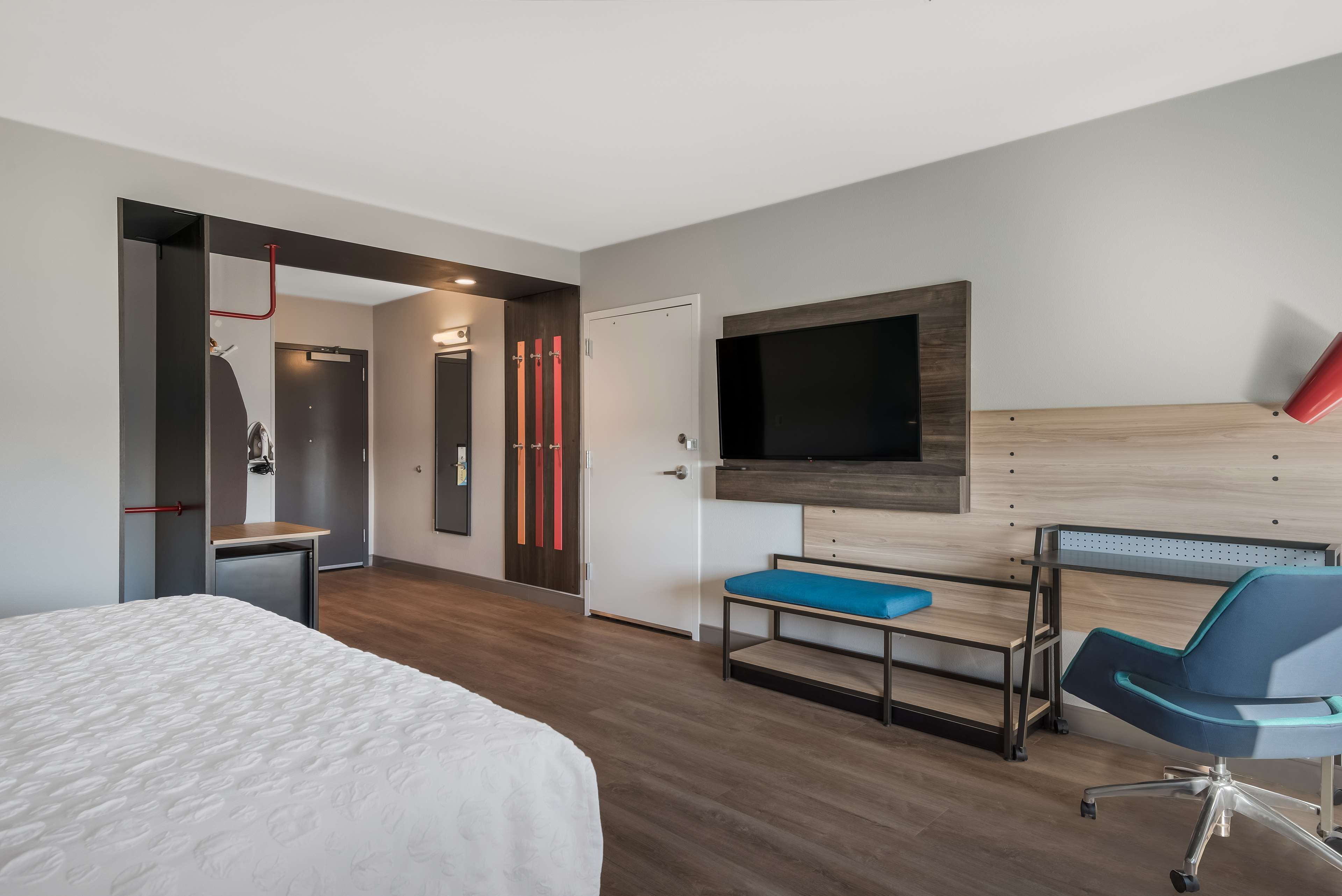 Une chambre d’hôtel moderne dotée d’un grand lit, d’un bureau avec une chaise, d’un téléviseur fixé au mur et d’une armoire avec un miroir.