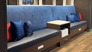Un espace salon moderne avec un canapé bleu à motifs, des coussins rouges et bleus, et une petite table sur laquelle se trouve une imprimante.