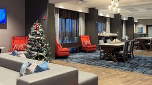 Un hall d’hôtel décoré d’un sapin de Noël, avec des fauteuils rouges, un canapé et un coin repas.