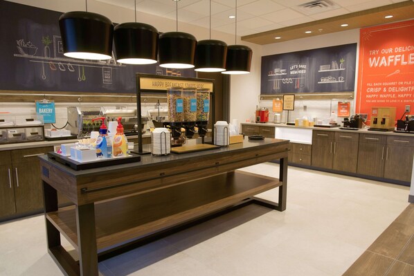 A bakery counter with coffee machines, a display of baked goods, and a sign advertising waffles.