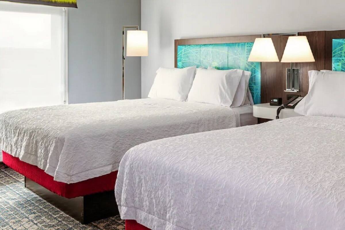 Une chambre d’hôtel avec deux lits, une table de chevet, une lampe et un mur décoré avec un motif de circuit imprimé.