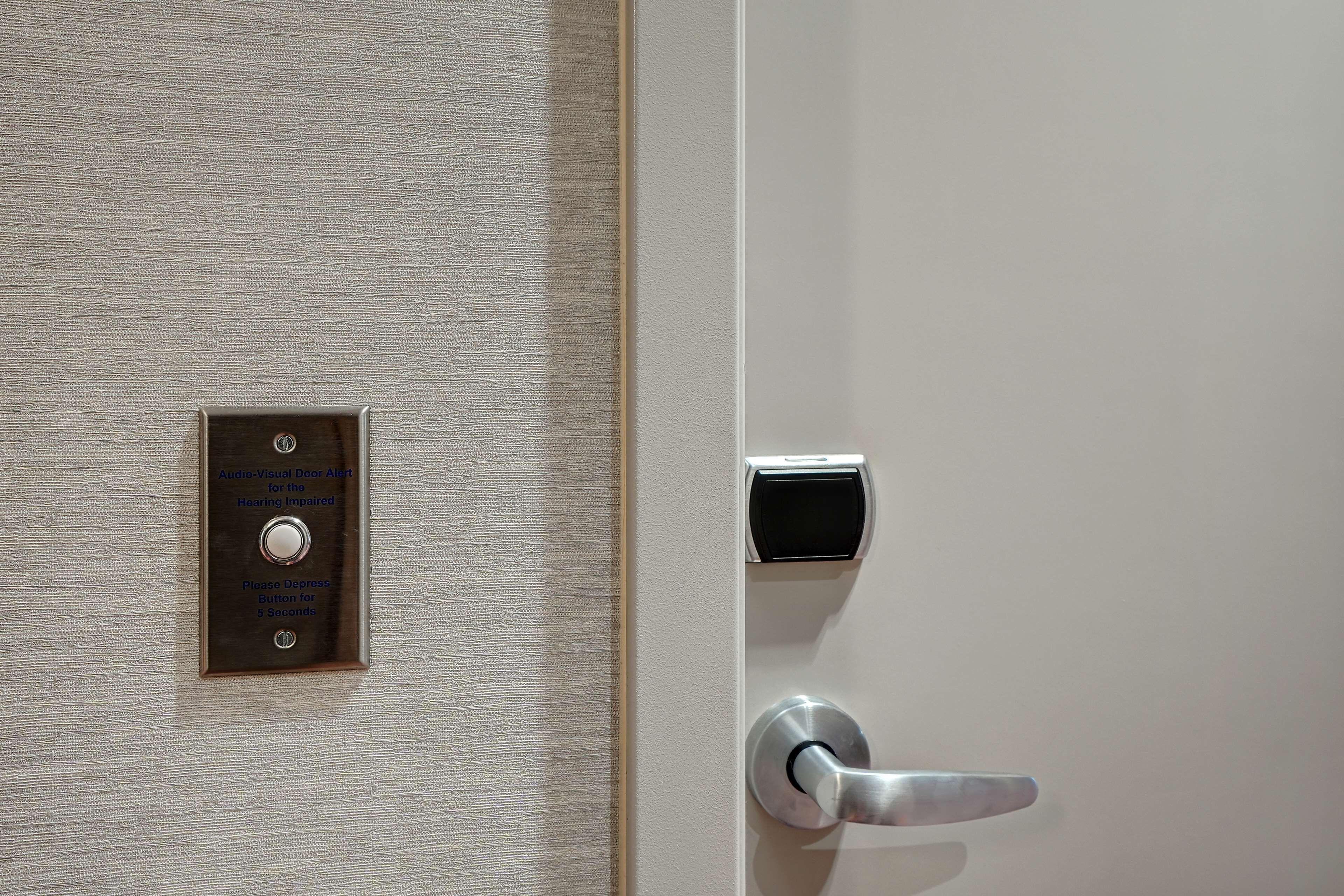 A door with a textured wall and a doorbell button labeled "Audio-Visual Door Alert for the Hearing Impaired."
