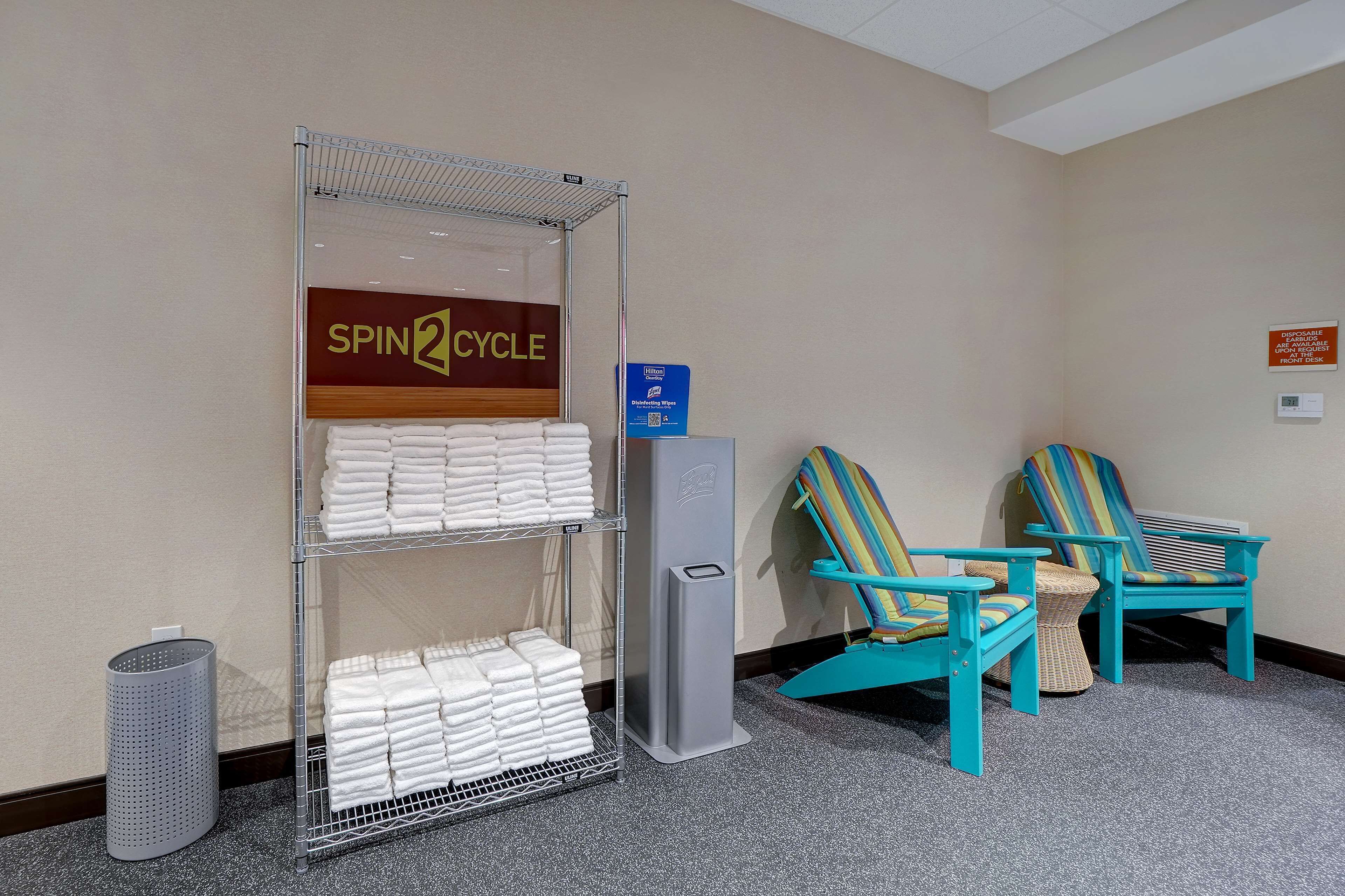 Una habitación con un cartel de 'Spin2Cycle', un contenedor de reciclaje y dos sillas a rayas.