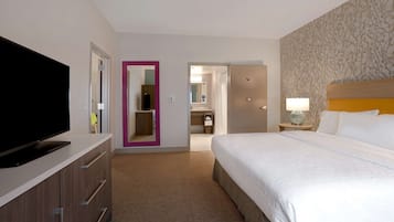 Habitación de hotel con cama, televisor, armario y baño visible a través de una puerta abierta.