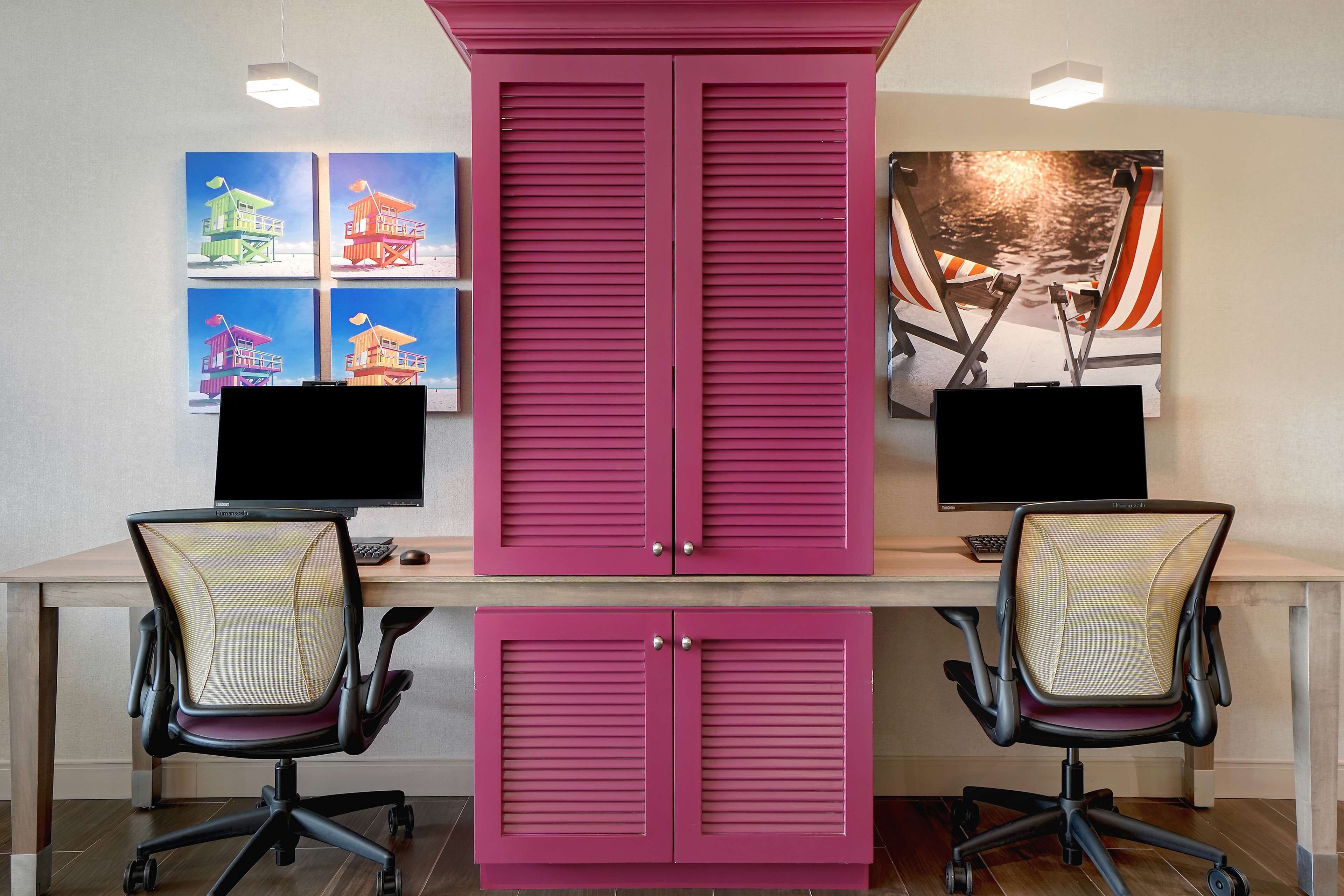 Un espace de travail comprenant deux bureaux, chacun équipé d’un écran d’ordinateur, de deux chaises de bureau et d’un grand meuble rose.