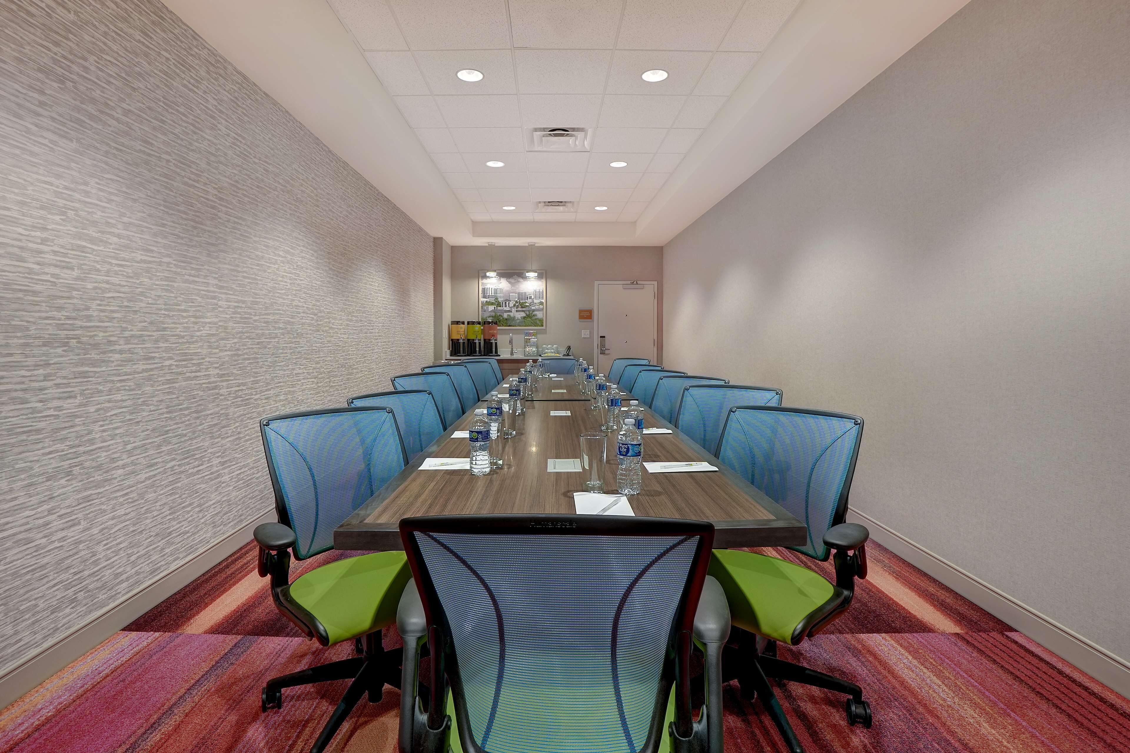 A conference room with a long table, blue chairs, and green chairs.