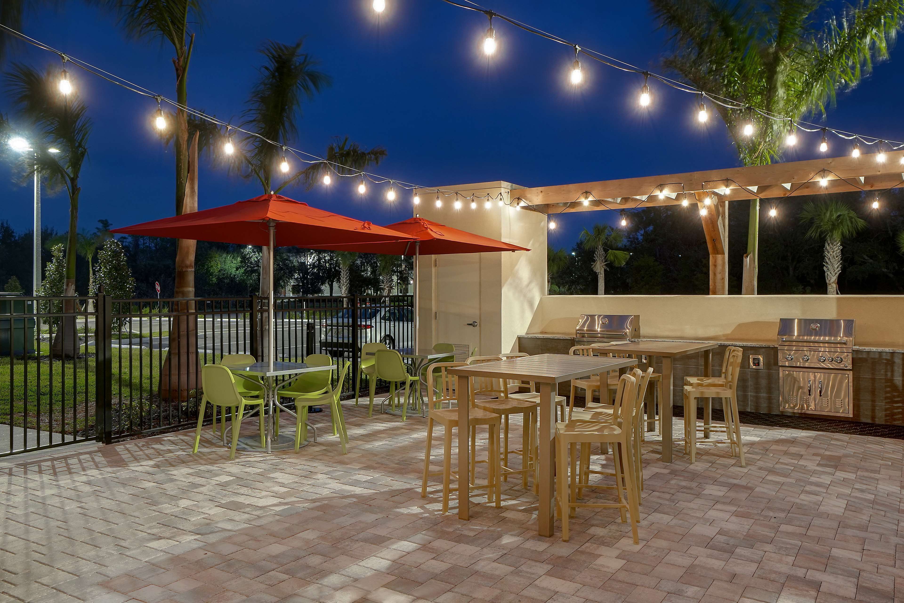 An outdoor patio with a wooden table and chairs, a barbecue grill, and string lights.