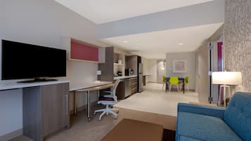 Una habitación de hotel moderna con televisión de pantalla plana, un escritorio, un sofá y una zona de comedor con sillas.