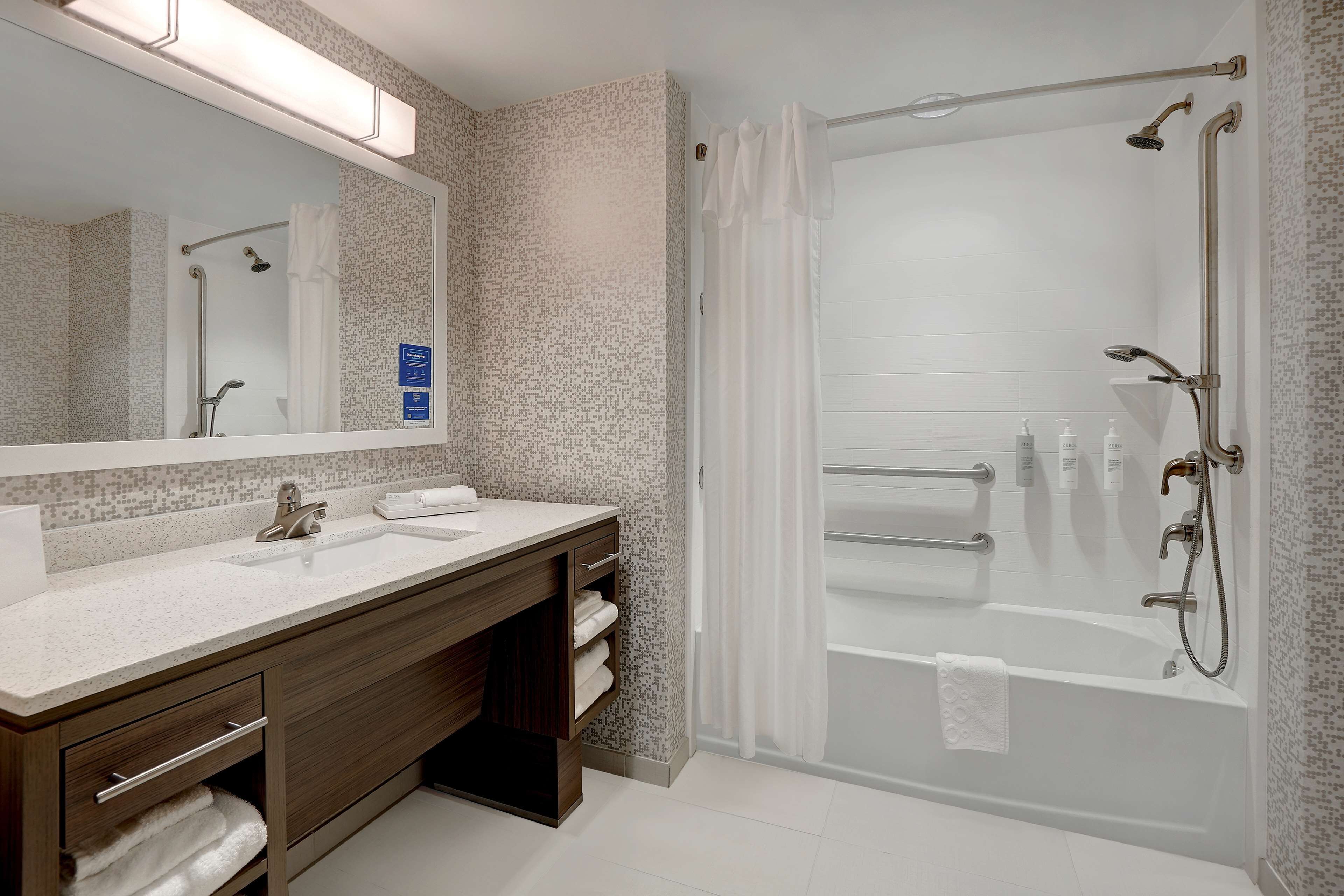 A modern bathroom with a large mirror, two sinks, a bathtub, and a shower.