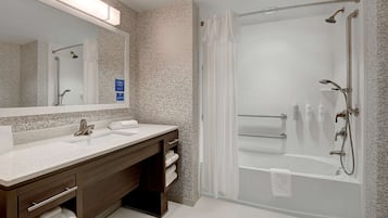 A modern bathroom with a large mirror, two sinks, a bathtub, and a shower.