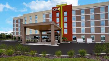 Un hotel moderno con ingresso coperto, diversi piani e un cartello ben visibile con la scritta 'Home 2'.